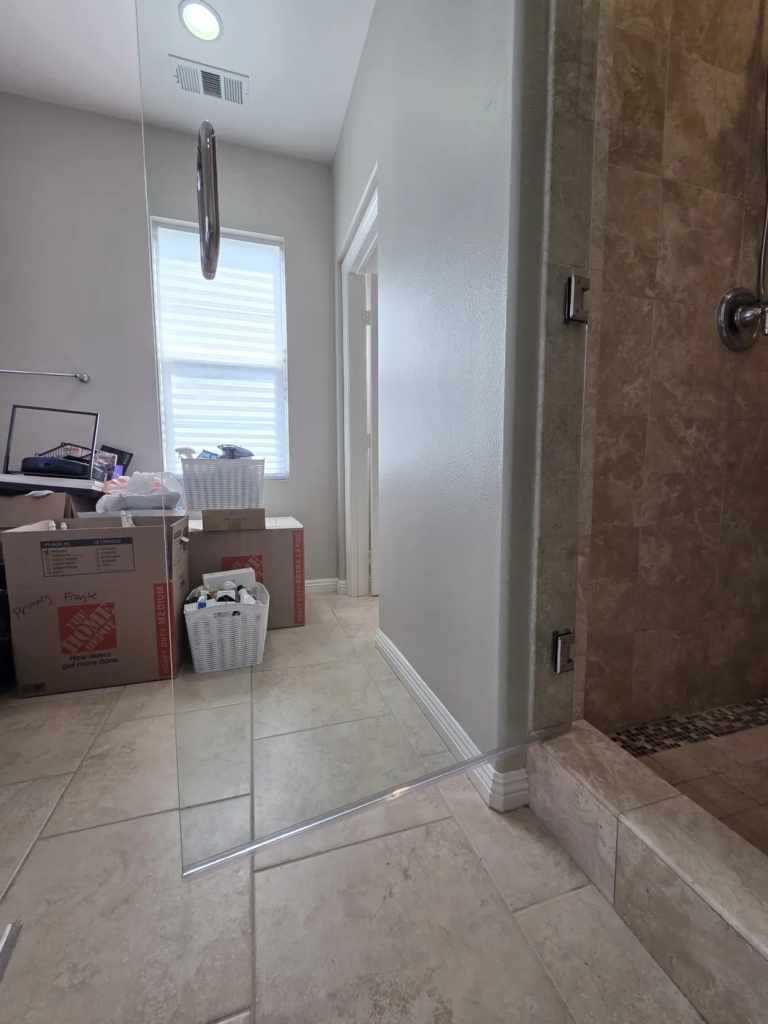 The same frameless shower door after service, clear enough to see the window, boxes and tile floor behind the glass