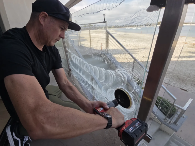 A Glass Revival technician polishing a stained exterior glass railing; the restored circles are clear while the surrounding glass is still clouded