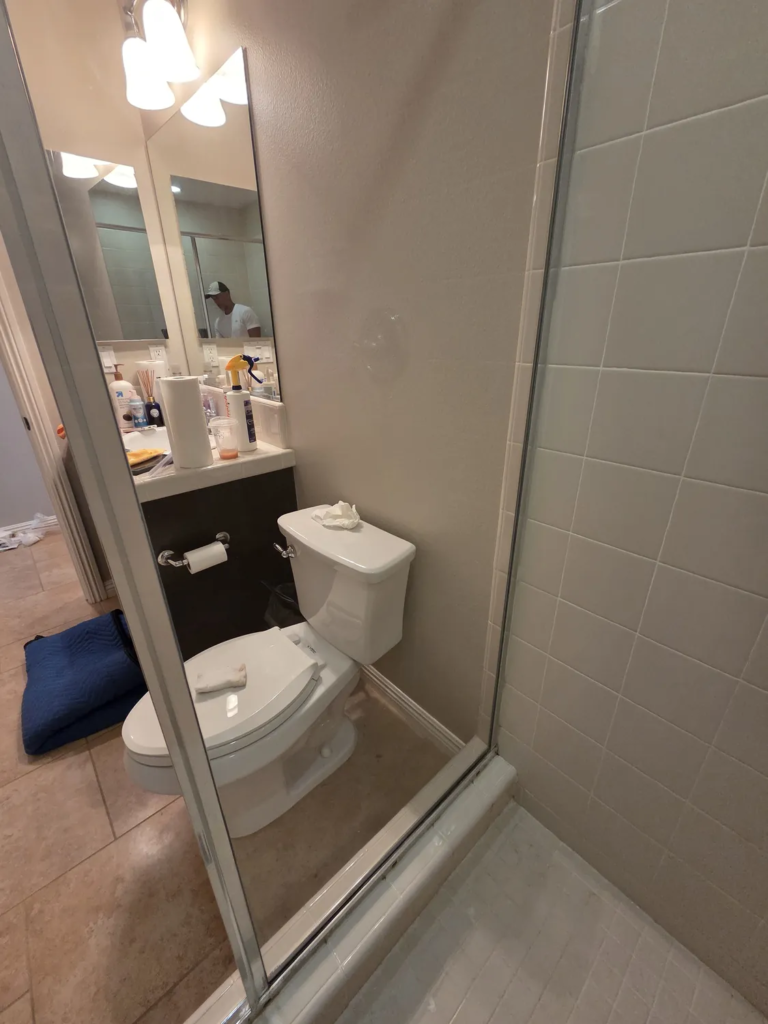 The same fixed shower panel after restoration, clear with the toilet and vanity visible behind it