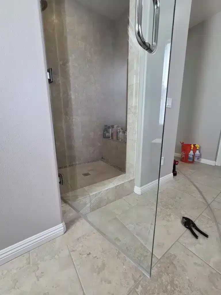 The same frameless shower door after restoration, clear enough to see the tiled shower and bench behind it