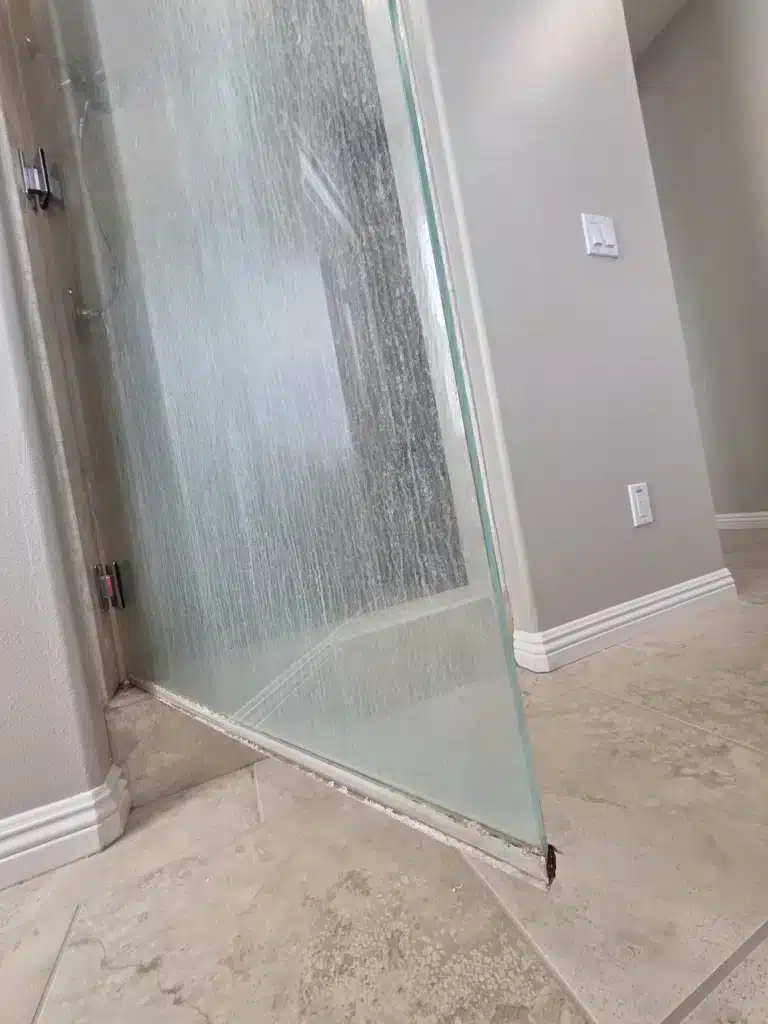 Frameless shower door before restoration, heavily clouded with white hard-water and mineral streaks